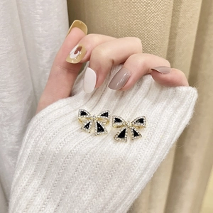 Macro view of dainty s925 gold bow earrings with black enamel and sparkling rhinestones