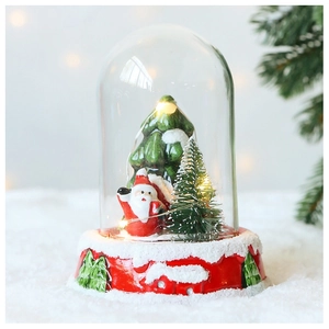 Detail of Santa Claus inside a lit glass dome with warm LED lights and snowy pine tree