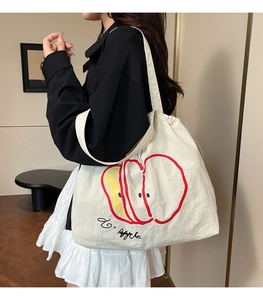 Detail of cream nylon tote bag with red apple print and drawstring closure on shoulder