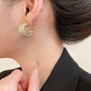Close-up of gold C-shaped hoop earrings with textured grain finish worn by model