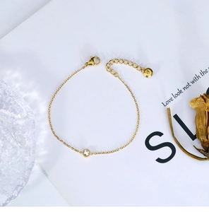 Detail of a gold bracelet featuring a single clear zircon and adjustable lobster clasp