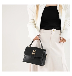 Close-up of black leather crossbody bag with gold double-ring clasp on white jacket