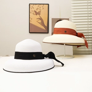 Close-up of wide brim straw hats with silk ribbons and metal M letter buckle detail