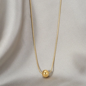 Elegant gold bead necklace with polished snake chain on grey silk background