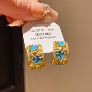 Gros plan détaillé de boucles d'oreilles créoles dorées avec fleurs bleues et zircons