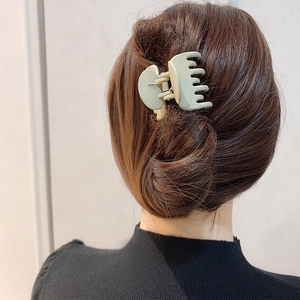 Detail view of a matte light green claw clip securing a high ponytail on brown hair