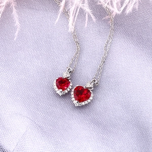 Close-up of heart-shaped red gemstone necklaces with silver chains on a satin surface
