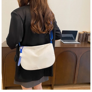 Detail of white nylon crescent bag with blue fabric strap and braided knot accessory