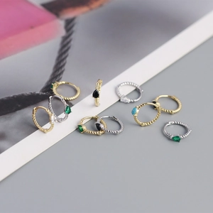 Macro shot of twisted huggie earrings with colorful pear-cut gemstones in gold and silver