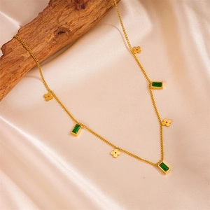 Detail of gold necklace featuring green rectangular gems and floral pendants on wood
