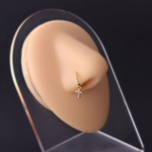 Close-up of golden cross pendant nose ring with zircon inlays on model display