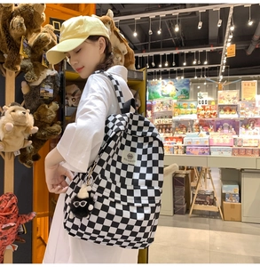Detail of checkered canvas backpack with fuzzy ball charm and brand logo patch