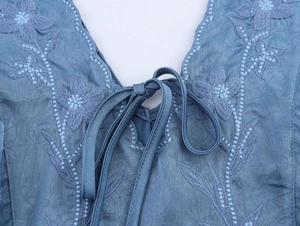 Détail de l'encolure avec broderie florale complexe et liens en soie bleue du vêtement