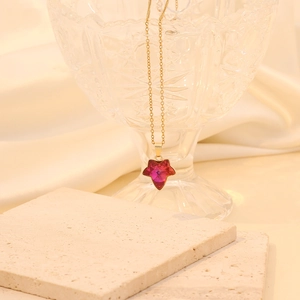 Collier doré élégant avec pendentif cristal étoile rouge suspendu sur un verre