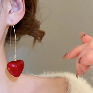 Detailed view of elegant red heart pendant earrings with gold hooks worn by a model