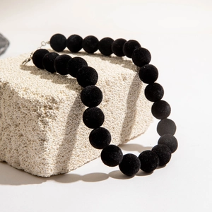 Vue détaillée du collier de perles noires à texture veloutée sur pierre décorative