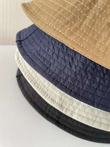 Close-up of stacked nylon bucket hats showing stitching detail in khaki navy white and black
