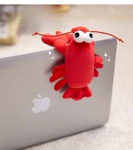 Close-up of a cute plush red crayfish toy clipped to a laptop for office desk decoration
