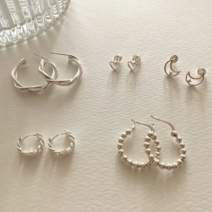 Flat lay of five pairs of 925 silver earrings featuring heart, moon, and twist designs