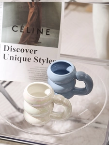 Close-up of cloud-shaped ceramic mugs in blue and pearlescent white on a glass table