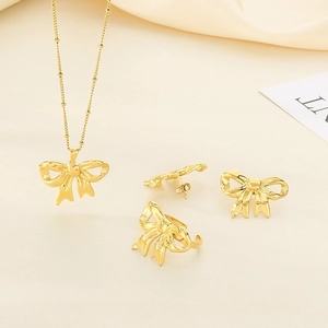 Golden bow jewelry set with pearl necklace, stud earrings and ring on silk background
