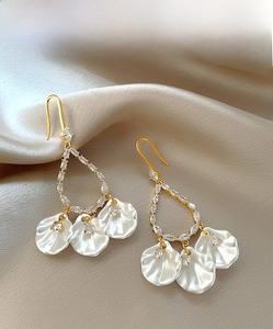 Détail de boucles d'oreilles dorées avec cristaux et pampilles coquillages sur soie beige