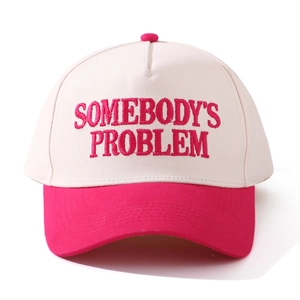 Close-up of pink 'SOMEBODY'S PROBLEM' embroidery on cream-colored baseball cap