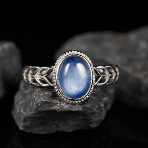 Macro shot of silver ring with oval blue gemstone and braided band on stone