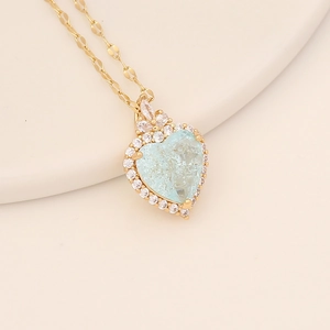 Detailed view of gold heart necklace with ice-cracked light blue stone and crystal halo