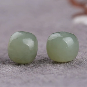 Macro view of two translucent light green Hetian jade beads on textured fabric