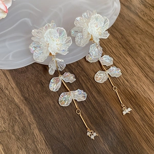 Detail of iridescent acrylic flower earrings with long tassel on a wooden desk