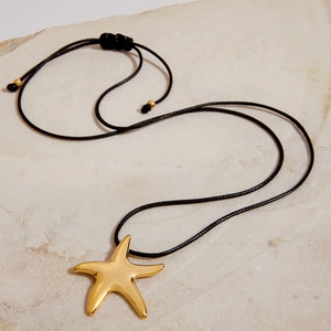 Macro shot of gold starfish pendant on black adjustable rope chain over textured stone