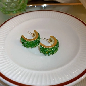 Detail of gold C-shaped earrings with green multifaceted crystals on a white ceramic tray