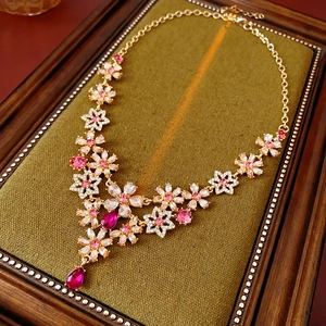 Macro shot of vintage gold flower necklace with pink crystal teardrop on green base