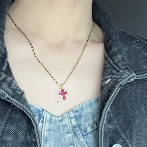 Detail of red zircon cross pendant necklace worn on neck with gold bamboo chain