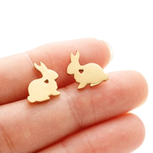 Detailed close-up of mini gold rabbit stud earrings with heart cutout held on a fingertip