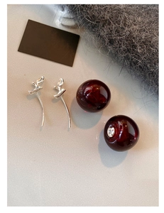 Detailed view of silver cherry-shaped earrings with dark red resin beads on grey fabric