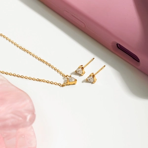 Dettaglio della collana placcata oro 18K e orecchini a cuore in zircone su sfondo chiaro