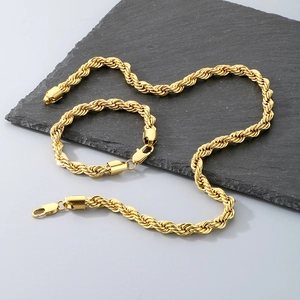 Détail d'un ensemble de collier et bracelet en chaîne torsadée dorée sur fond de pierre