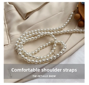 Detail shot of an elegant pearl shoulder strap with gold metal clasps on beige fabric