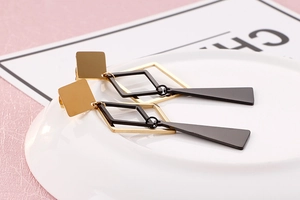 Detail of geometric long earrings with gold square studs and black triangular pendants