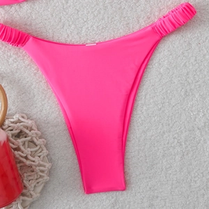 Détail du bas de bikini échancré rose fluo avec côtés froncés sur tissu texturé