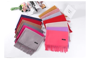 Flat lay of cashmere scarves in multiple colors like pink, red, and blue with fringe detail
