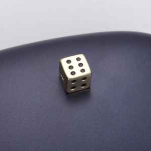 Macro shot of a golden dice pendant bead with black dots and a through-hole for jewelry DIY