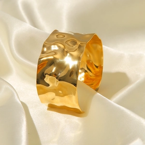 Close-up of golden wide open cuff bracelet with a hammered texture on white silk fabric