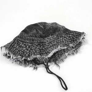 Detail of black washed denim bucket hat with frayed edges and cross metal pin ornament
