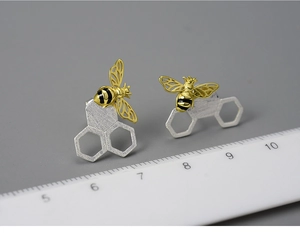 Macro detail of silver honeycomb bee earrings next to a ruler showing small scale size