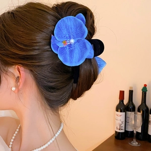 Detail of blue orchid hair claw clip with pearl center worn on a textured bun hairstyle