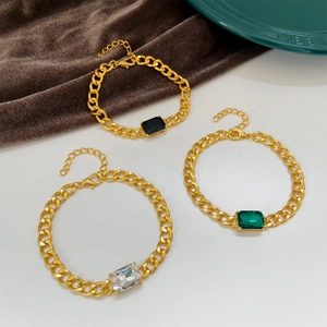 Detail of chunky gold Cuban chain bracelet with emerald green and black zircon stones