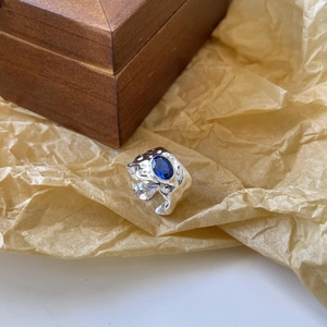 Detailed macro view of wide irregular silver ring with blue oval stone on wood background